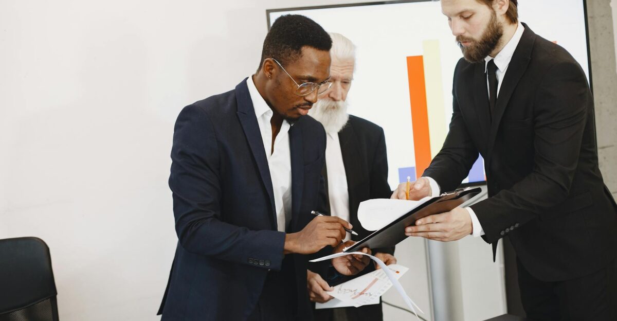 Three businessmen engaged in document signing in a modern office setting