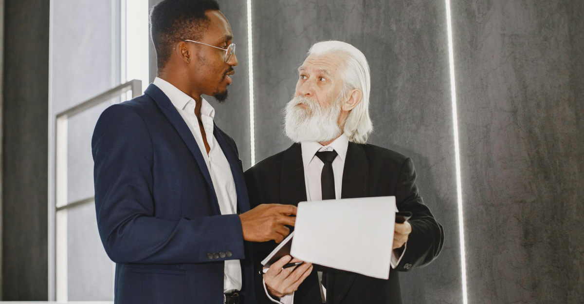Two businessmen in suits discussing documents indoors on modern stairs.