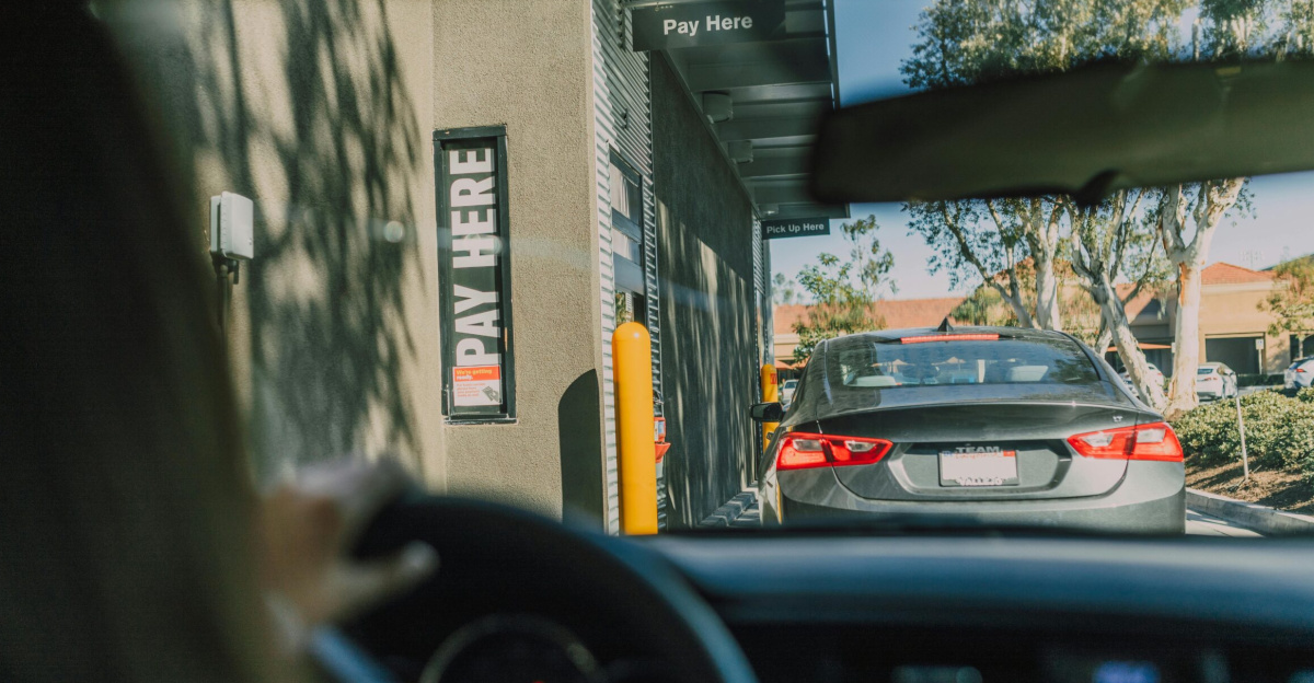 A driver's perspective waiting at a fast food drive-thru queue in daylight.