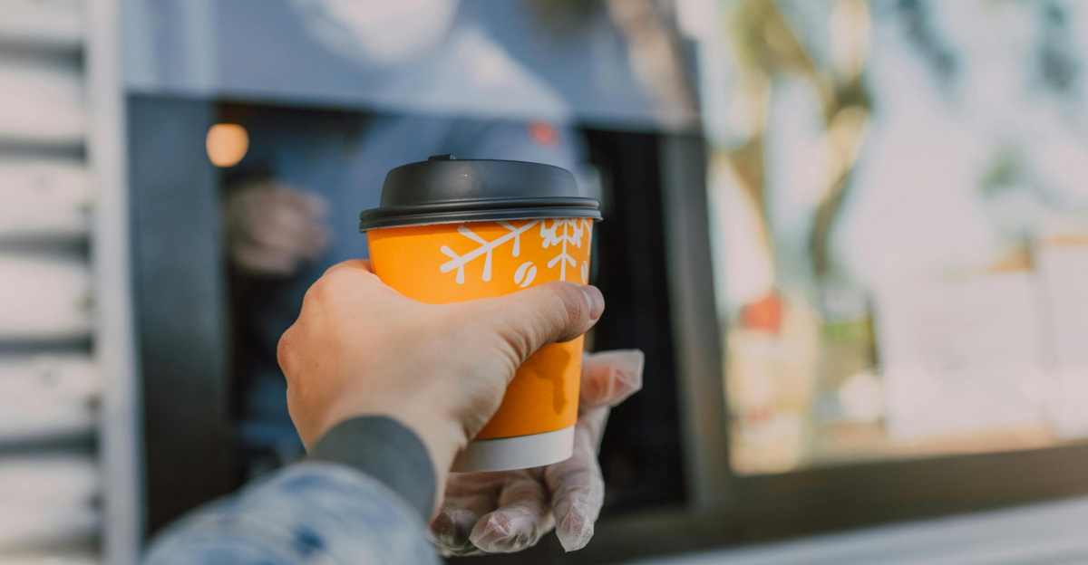 Hand reaching out for a hot coffee cup at a drive-thru window, depicting everyday convenience.