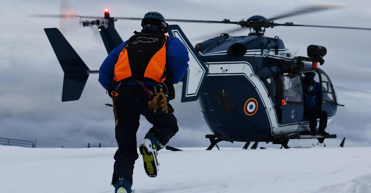 Rescue worker approaches helicopter on snowy field for emergency response.