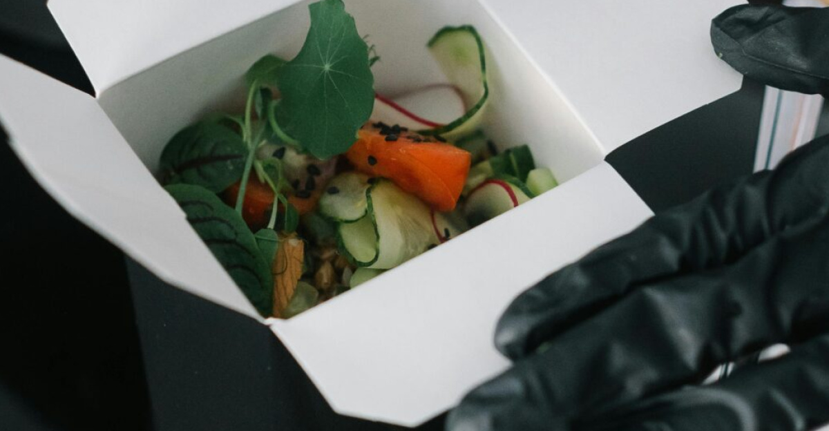 Gloved hands preparing fresh salad takeout in eco-friendly containers for delivery.