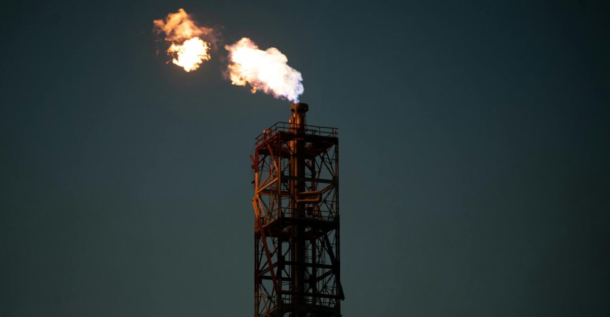 A towering industrial chimney with a dramatic flame against a dark sky in Salina Cruz Mexico