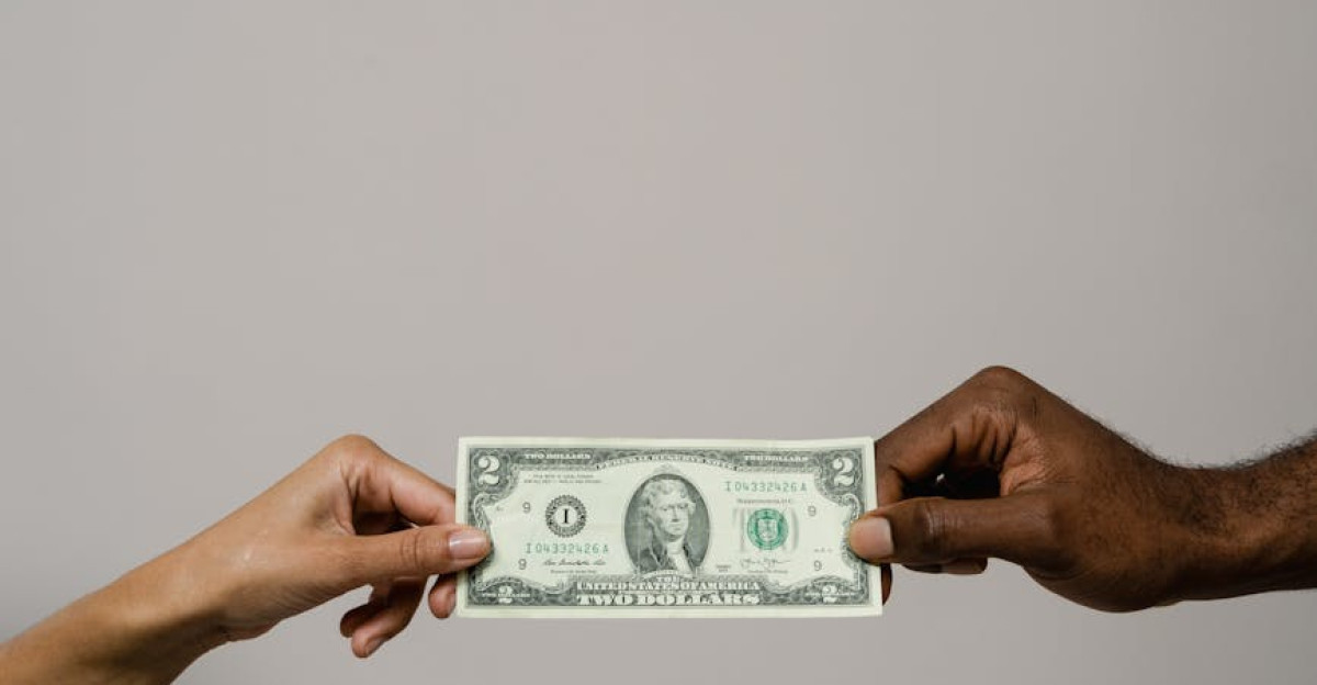 A dollar bill is exchanged between two diverse hands on a neutral background