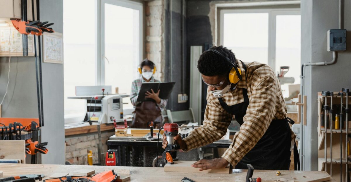 Carpenter using tools in a workshop with a colleague in the background