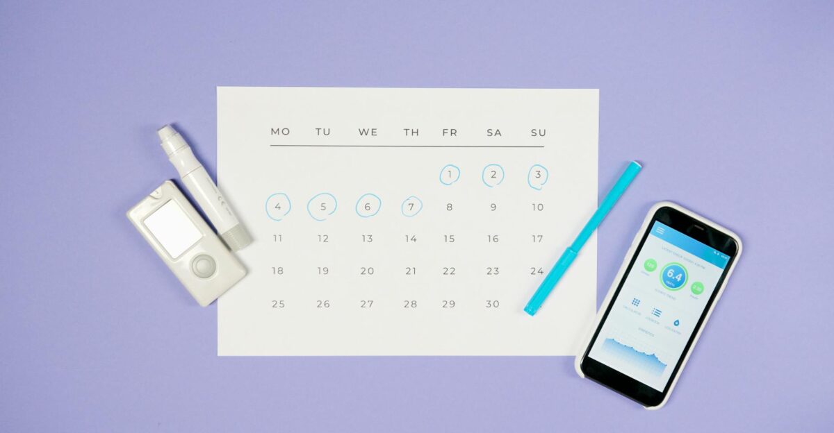 Flat lay of calendar with medical devices and smartphone representing diabetes management