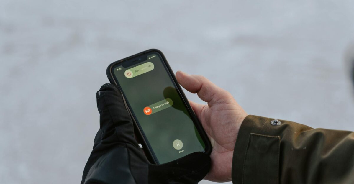 Gloved hands holding a smartphone displaying an emergency SOS screen
