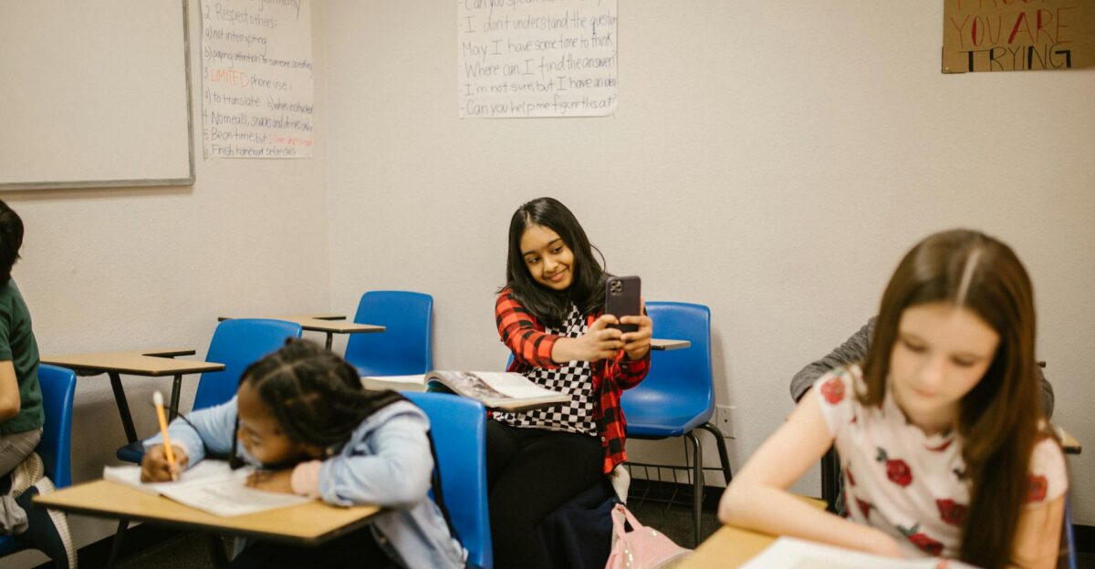 A diverse group of students in a classroom setting one using a smartphone