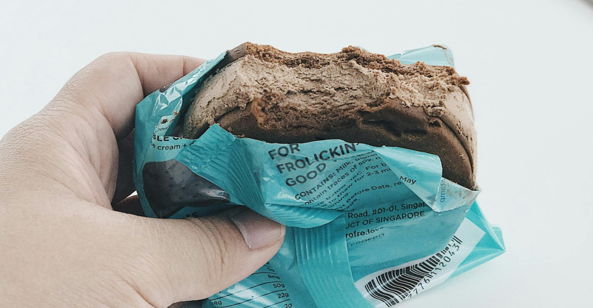 Close-up of a hand holding a chocolate ice cream sandwich in turquoise packaging.