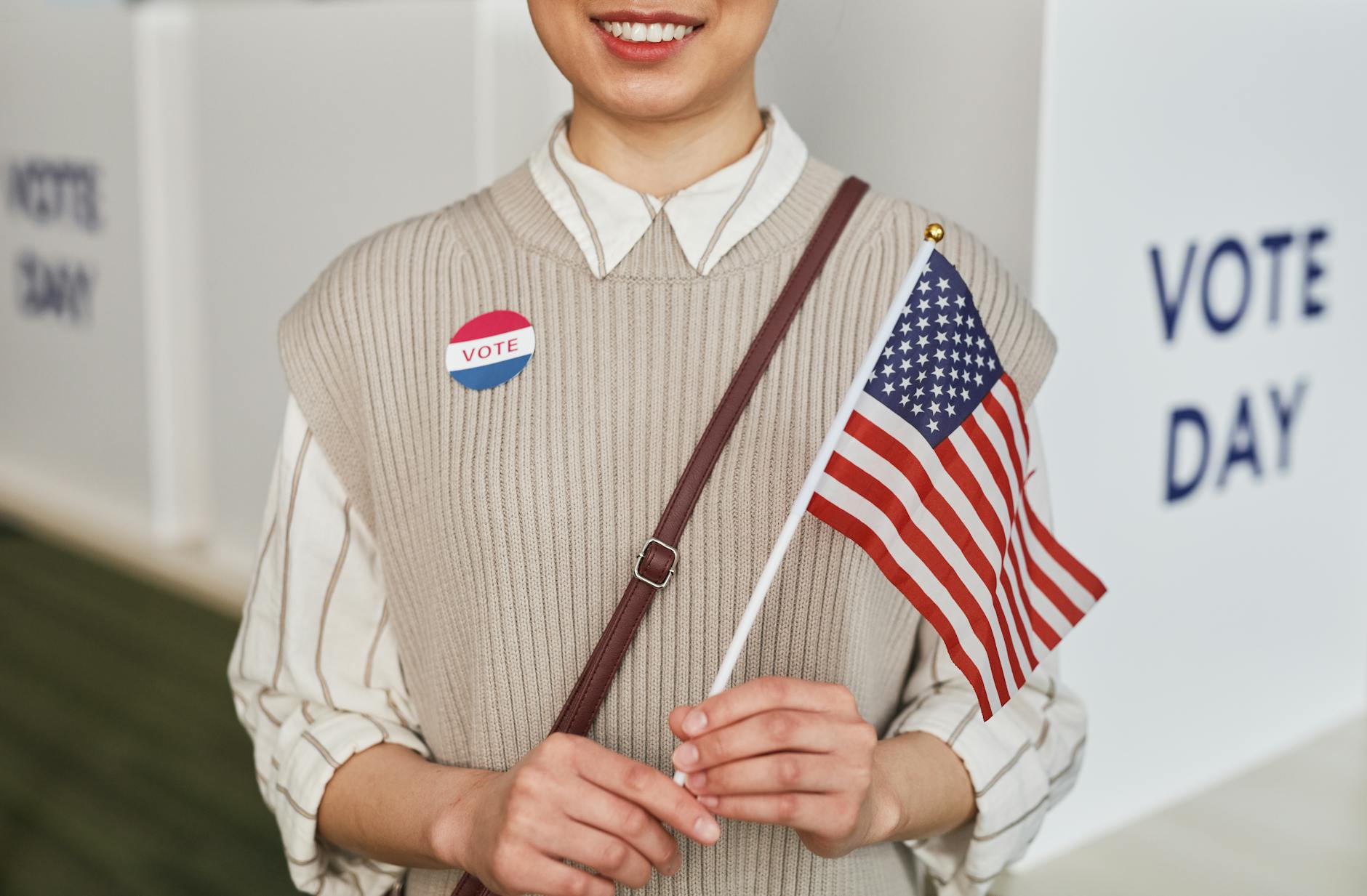 A woman proudly holds the American flag and smiles celebrating voting day