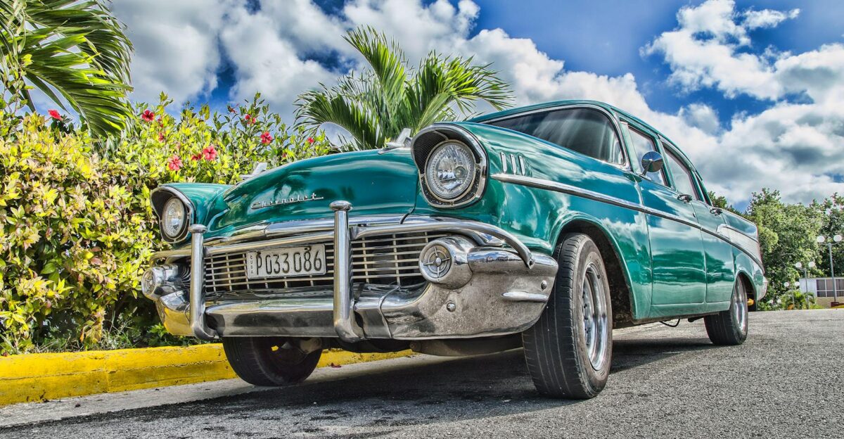 A beautifully restored classic car on a sunny road in Havana Cuba with lush foliage and a vibrant sky