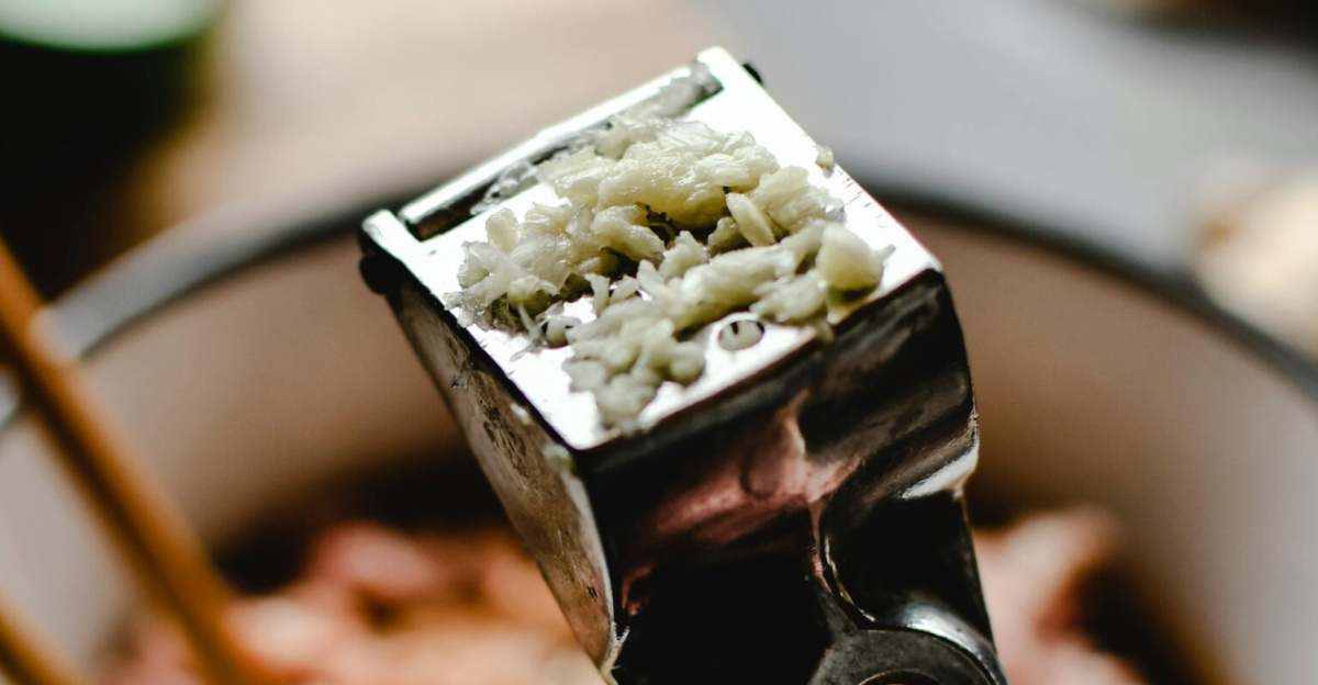 Freshly pressed garlic in a stainless steel press with a cooking background.