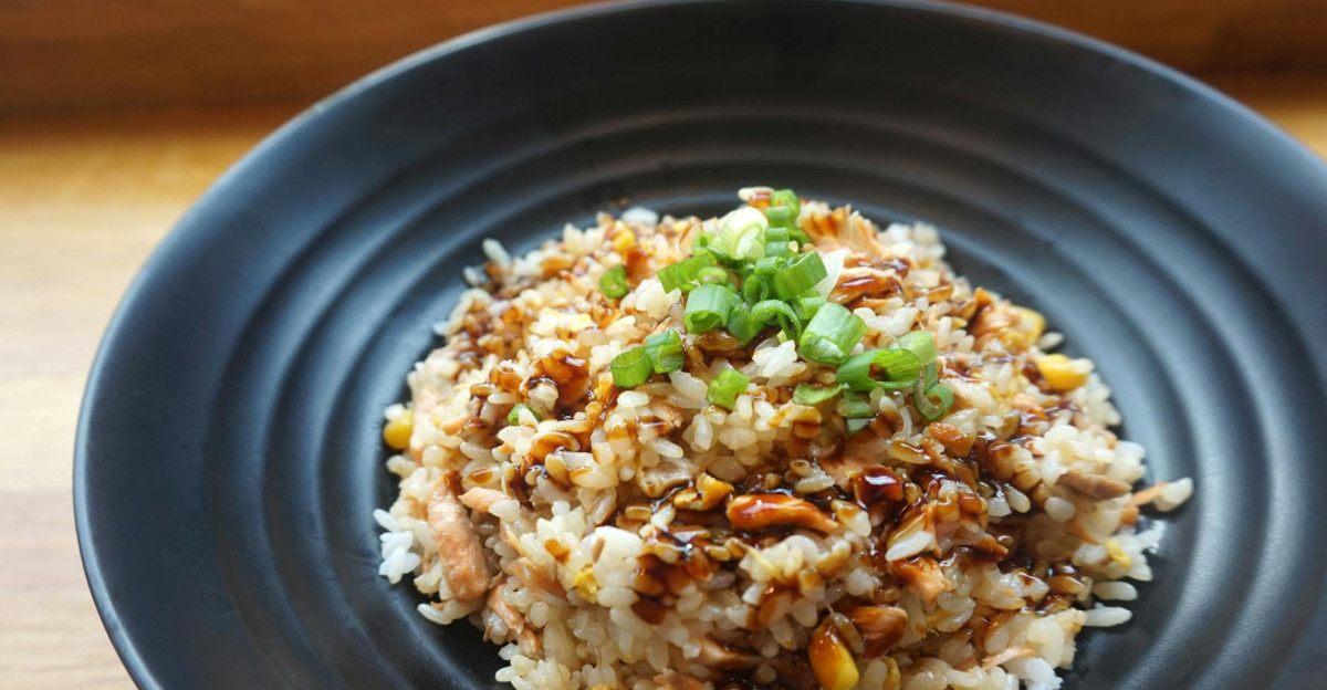Delicious homemade fried rice with scallions and sauce on a black plate