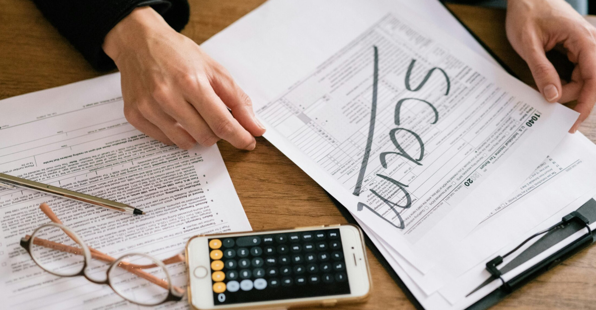 Hands of a person examining tax forms labeled as scam with calculator and papers.