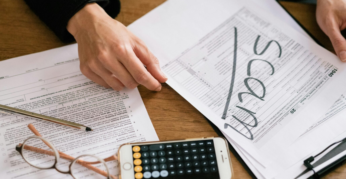 Hands of a person examining tax forms labeled as scam with calculator and papers.