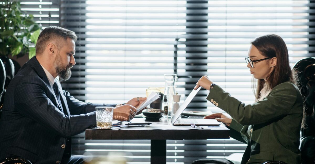 Professional business meeting with two colleagues discussing over laptops and documents in a stylish office setting