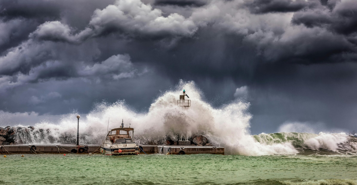 Powerful waves crash against a pier and lighthouse under dark stormy skies.