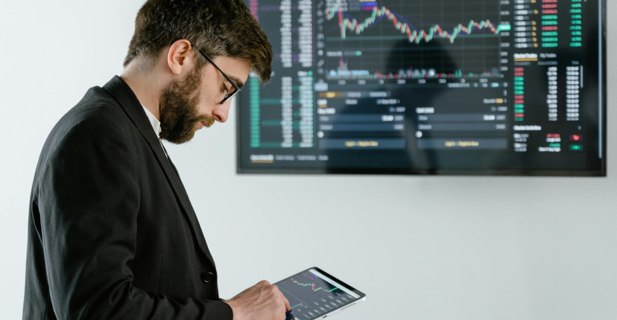 Professional man using tablet in front of cryptocurrency trading screen indoors.