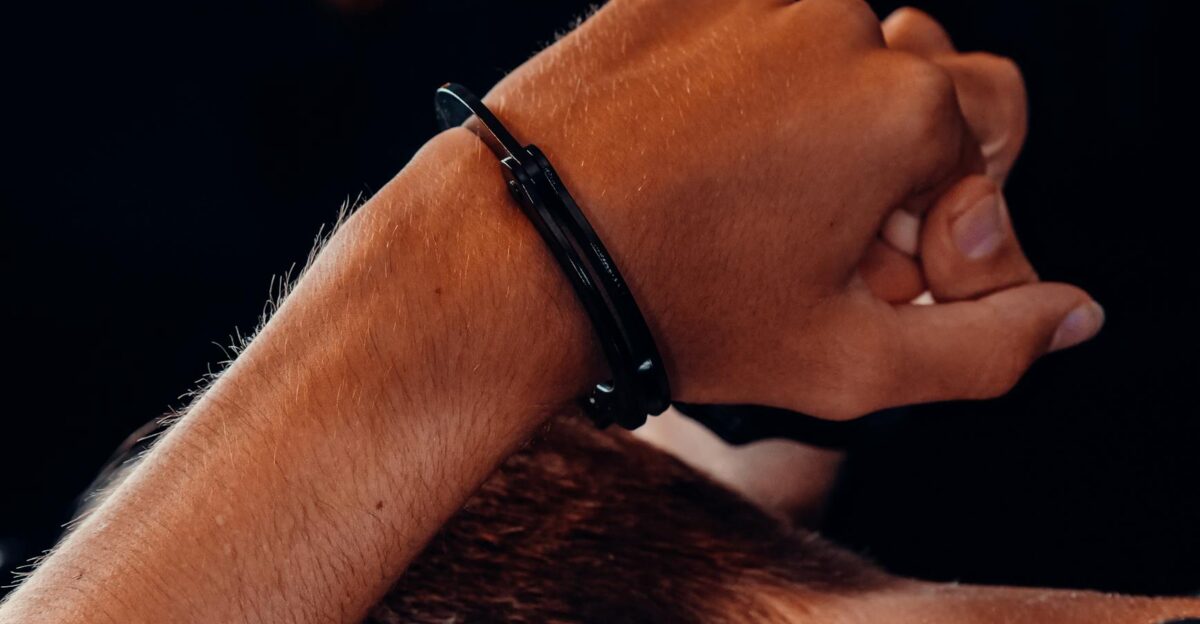 A close-up of a hand in handcuffs against a dark background depicting a concept of security and restraint