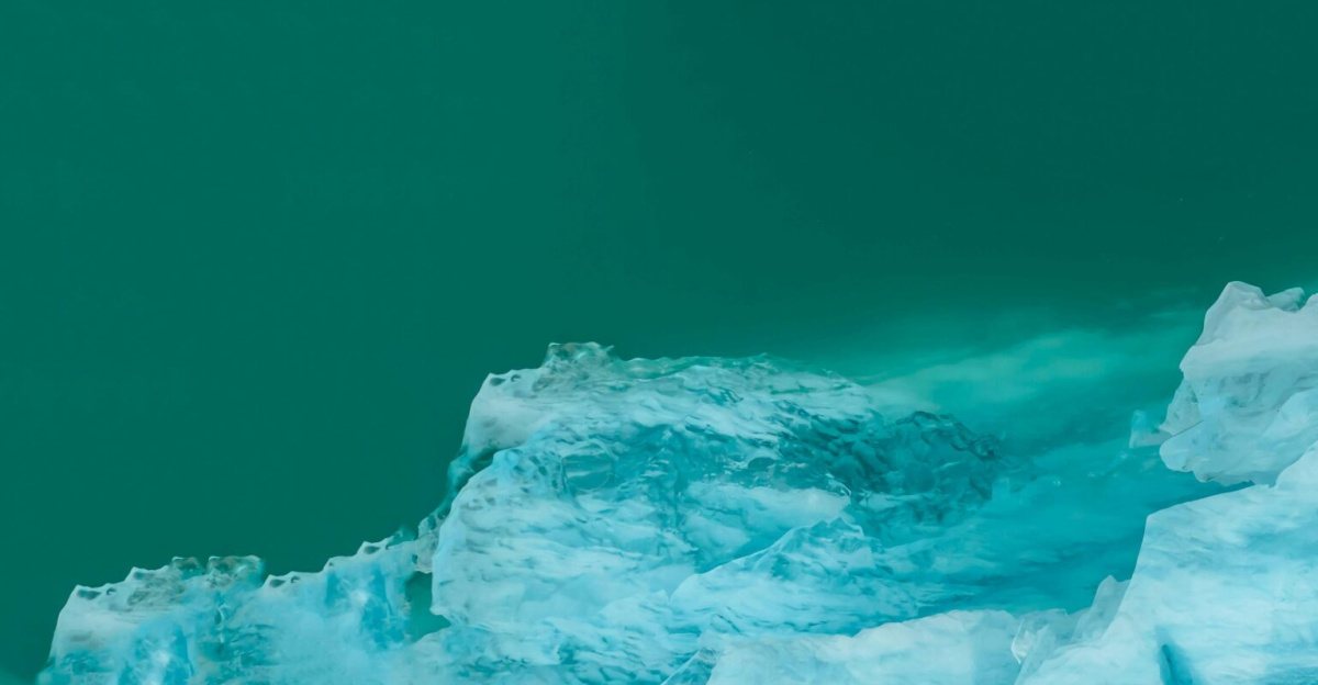 A stunning aerial shot of a blue iceberg floating in the cold sea water.