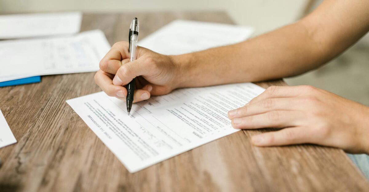 Hand filling out paperwork with a pen showcasing focus on document completion