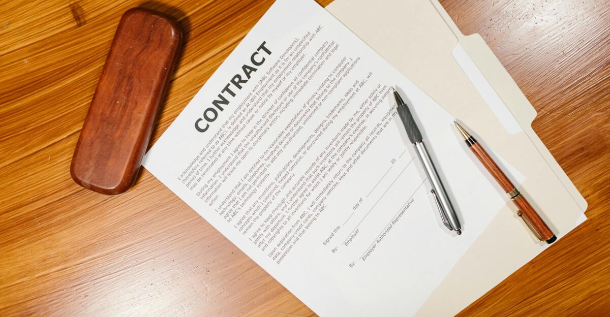 High-angle view of a contract document with pens and a case on a wooden table