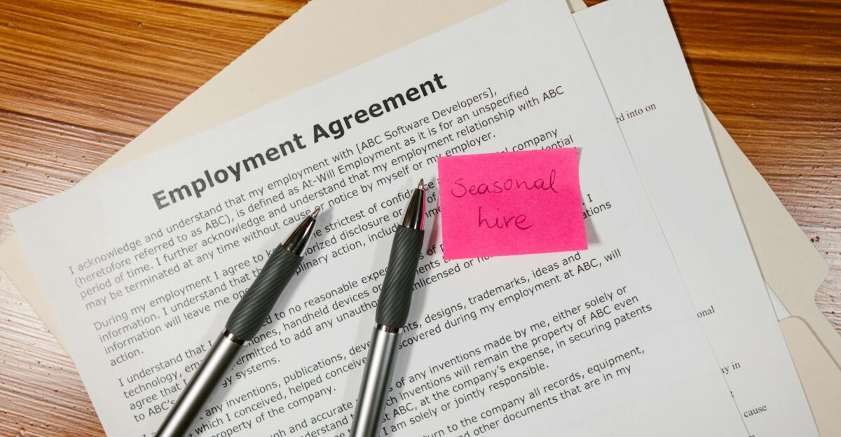 Top view of employment agreement contract with pens and seasonal hire note on wooden desk