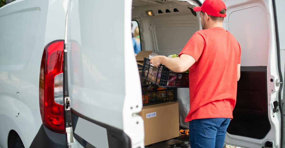 A courier in a red cap loads a delivery van with packages and a basket outdoors in Portugal