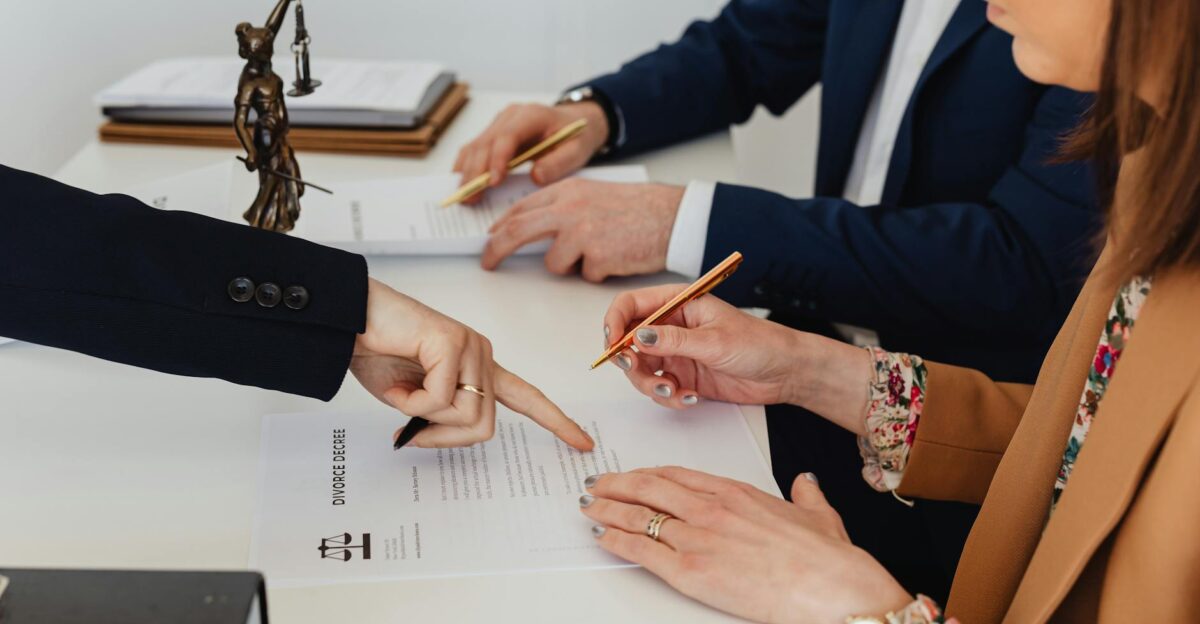 Hands signing a divorce decree with a justice statue nearby symbolizing legal proceedings