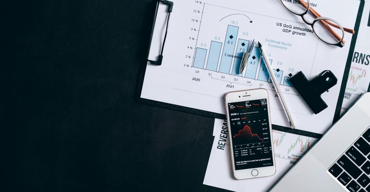 Top view of financial reports smartphone showing stock market data and a laptop on desk
