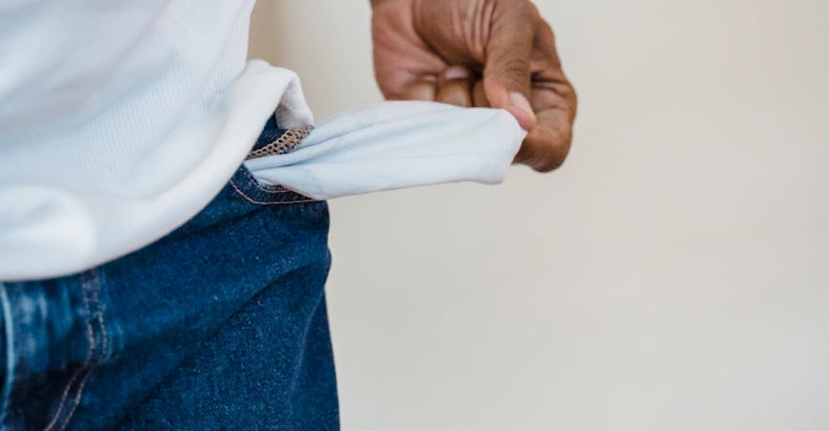 A person in jeans reveals an empty pocket symbolizing financial hardship