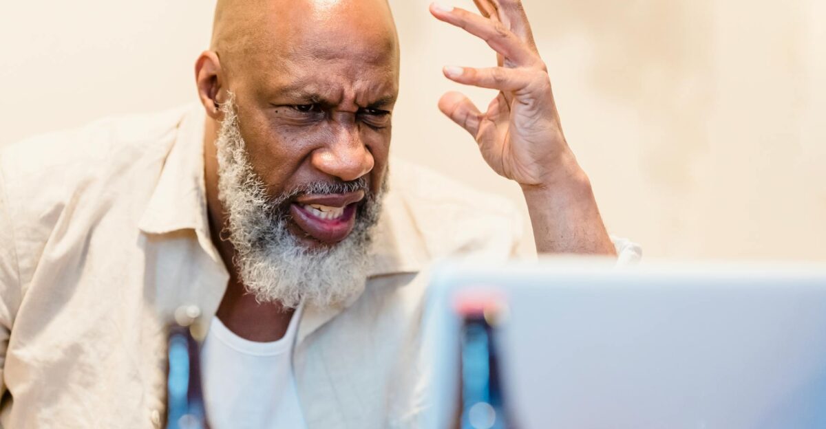 An adult man expressing frustration during a video call with a laptop indoors