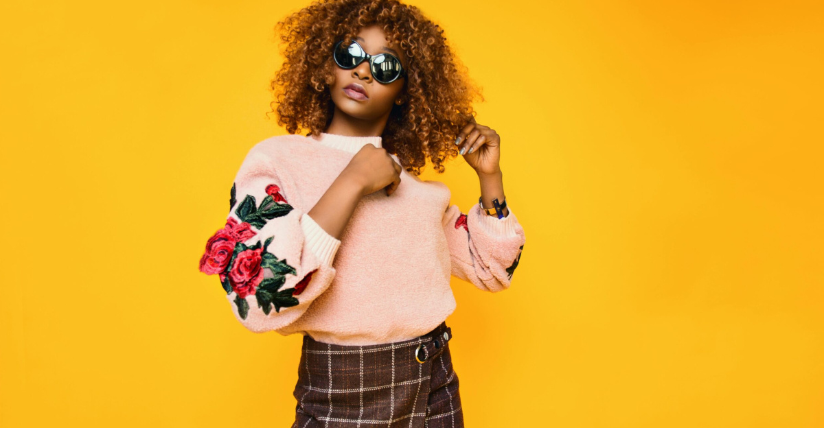 Chic woman with afro hair in a floral sweater and plaid skirt posing confidently.