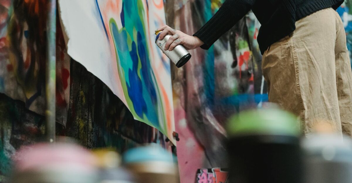 Artist using spray paint to create vibrant graffiti on canvas indoors