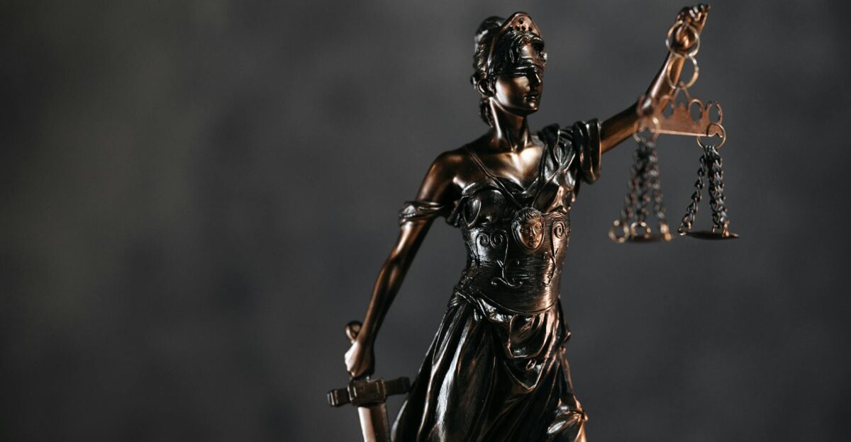 Detailed bronze Lady Justice statue with scales and sword against a dark background symbolizing law and justice