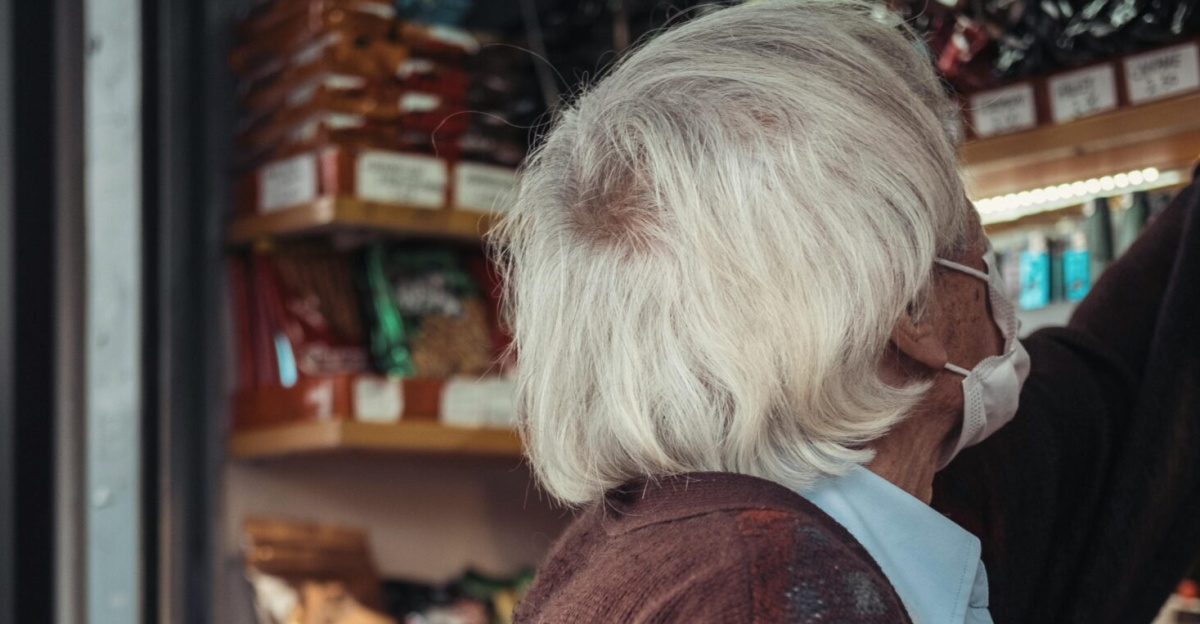 Senior adult in a protective mask selecting items in a store aisle during the pandemic.