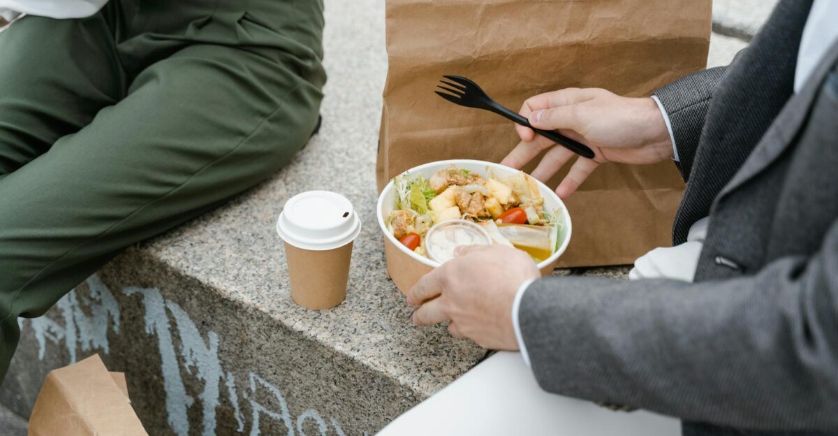 Two people enjoying a takeaway salad and coffee outdoors seated on a stone bench