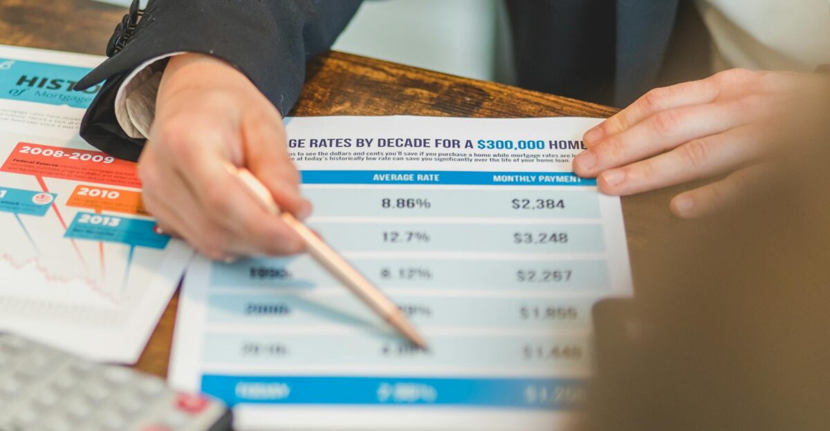 A close-up of hands analyzing mortgage rate documents with a pen and calculator in a business setting
