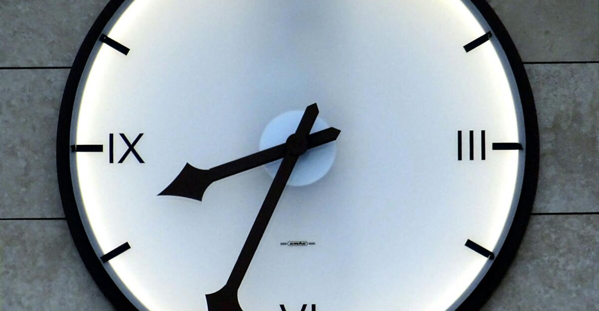 Close-up of a modern wall clock with Roman numerals and backlit design emphasizing timekeeping precision