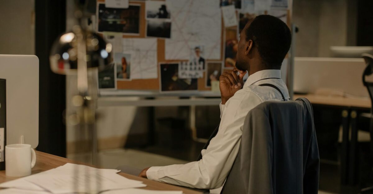 Detective in thought examining evidence board in a dimly lit office environment