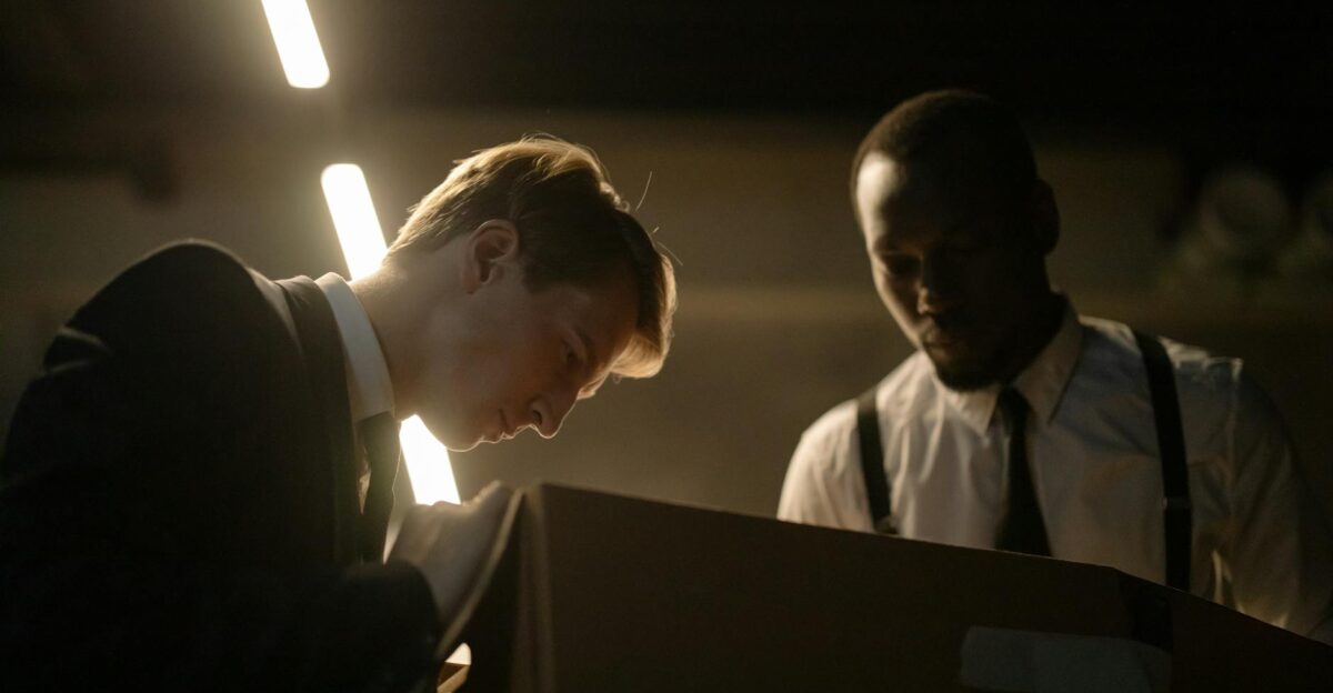 Two detectives examine a box in dimly lit room focused on investigation