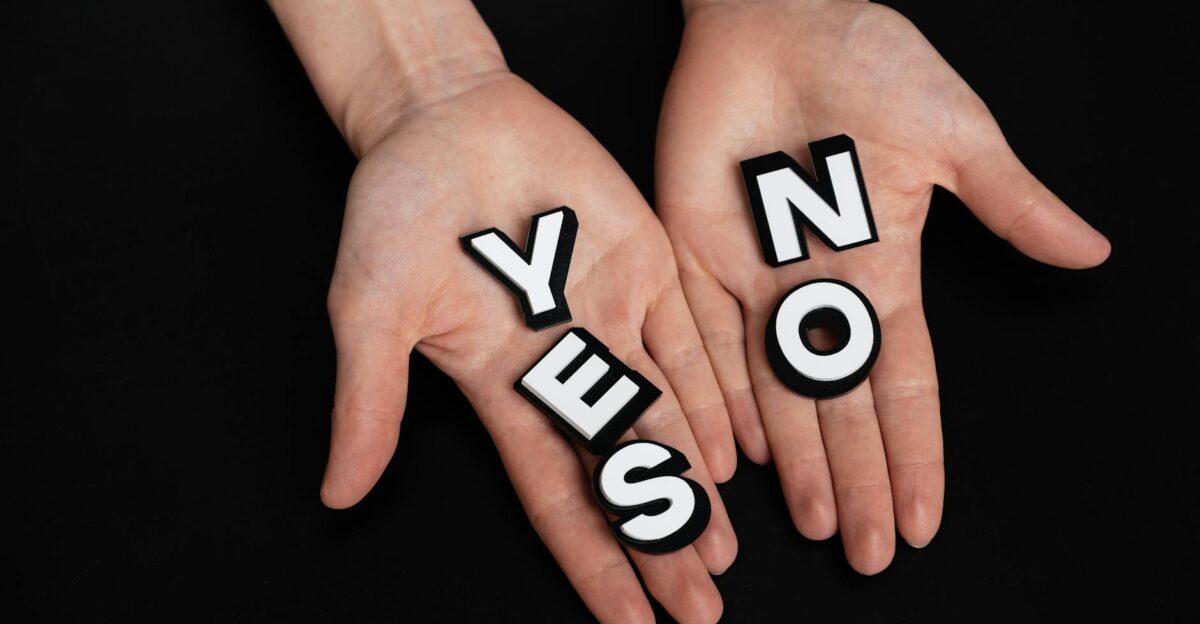 Two hands holding black and white letters spelling YES and NO on a black background