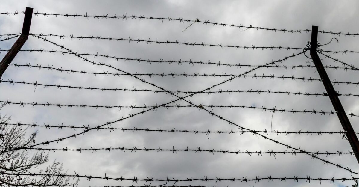 Dramatic low-angle view of a barbed wire fence silhouetted against a cloudy sky