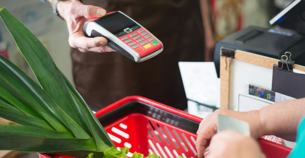 A customer using a contactless payment method at a grocery store checkout with fresh produce.