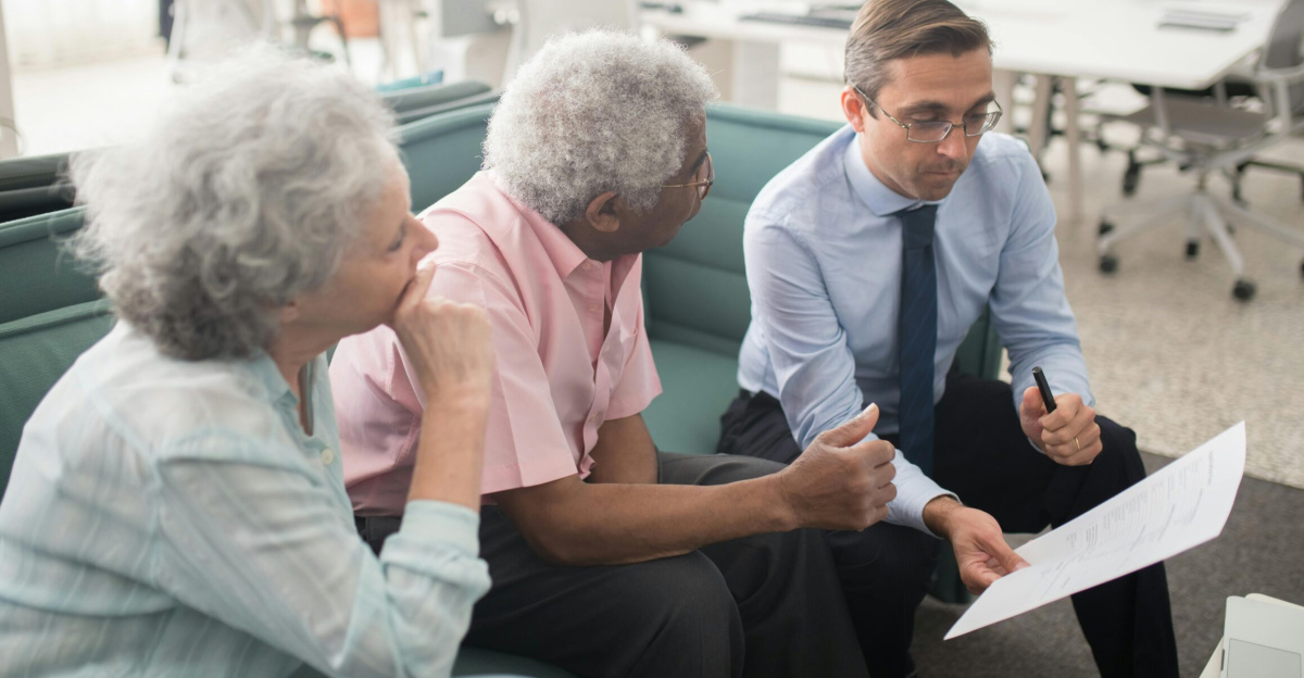Business professional consults elderly clients in an office setting. Collaborative discussion, paperwork visible.