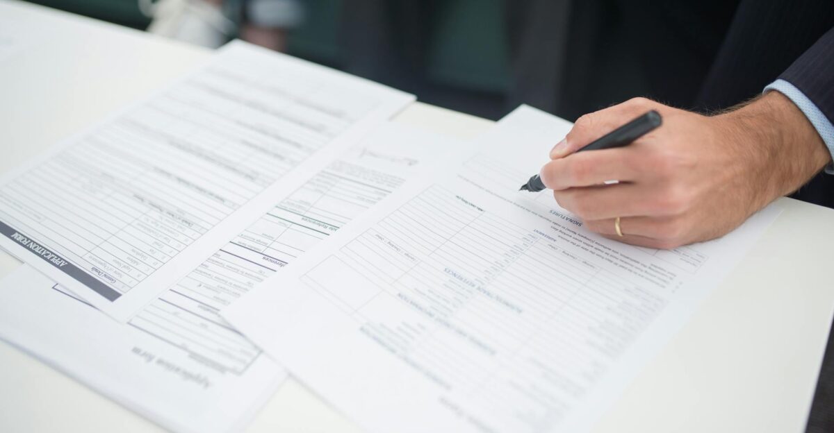 Close-up of a hand signing insurance documents in an office setting