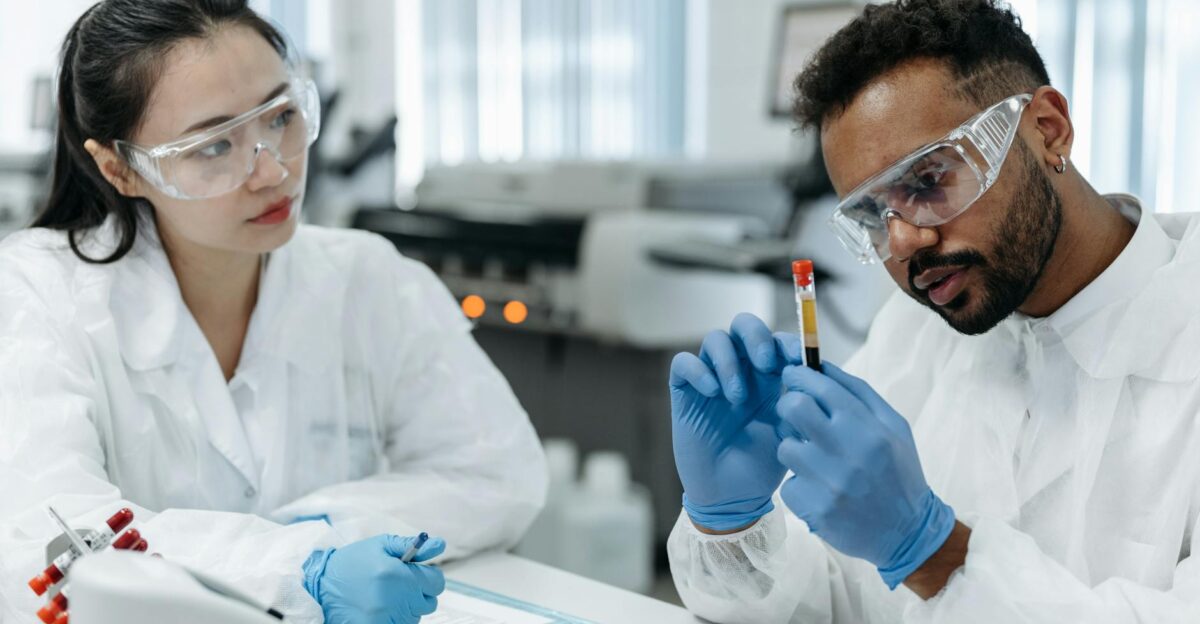 Two scientists in protective gear analyze blood samples in a laboratory setting