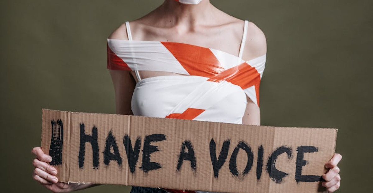Woman wrapped in tape holding a sign saying I Have a Voice symbolizing protest and speech suppression
