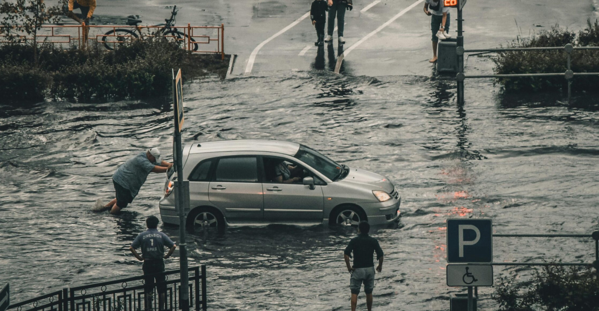 A flooded city street with a car being pushed and pedestrians navigating the water.