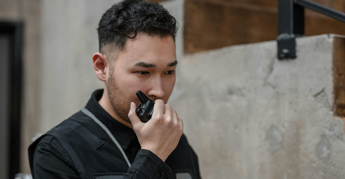 Asian security guard using walkie talkie in an indoor setting, demonstrating communication and alertness.